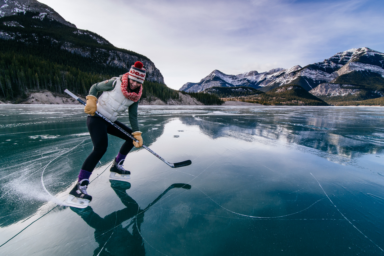 Une patineuse, avec son bâton de hockey, s'amuse sur le lac Barrier, en Alberta. Le lac est entouré de glaciers.