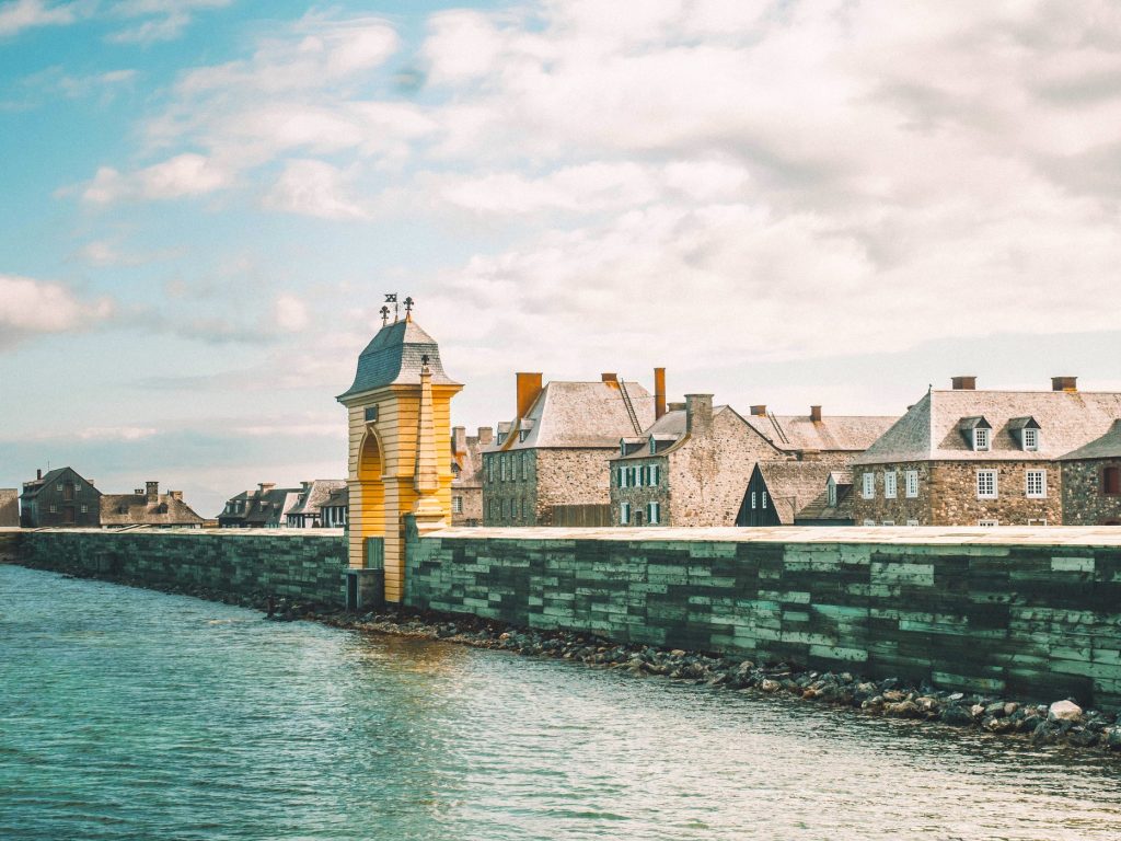 De l'eau, se dresse la forteresse de Louisbourg : des bâtiment de pierre, dont l'auberge, des résidence. On devine un village imposant.